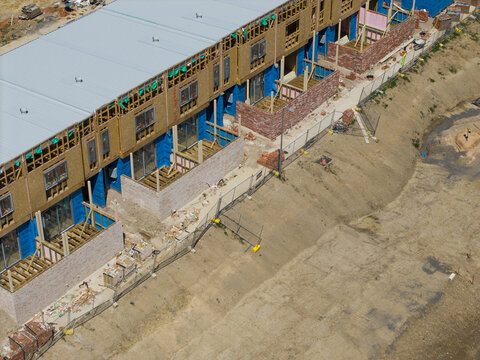 Melbourne, Victoria, Australia - 08 October 2026: Aerial view of a residential construction site with rows of partially built townhouses, wooden framing, brick foundations, and blue protective wrap.