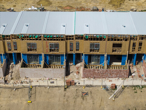 Melbourne, Australia - 08 October 2026: Aerial view of a residential construction site featuring rows of townhouses with metal roofs, wooden framing, and brick foundations.