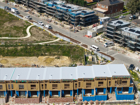 Melbourne, Australia - 08 October 2026: Aerial view of a residential construction site featuring rows of townhouses under development with wooden frames and blue protective wrap.