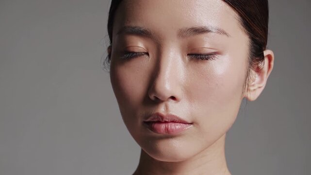 Young woman looks directly forward with calm serene expression during beauty studio portrait session. Model maintains gentle gaze while subtle studio lighting emphasizes flawless skin texture.