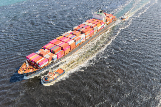 Fremantle, Australia - 06 October 2022: Aerial view of a large container ship being guided by tugboats through the deep blue water of Fremantle Harbour.