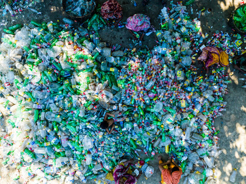 Narayanganj, Bangladesh - 09 November 2024: Aerial view of workers sorting a large pile of discarded plastic bottles for recycling in a waste management facility.