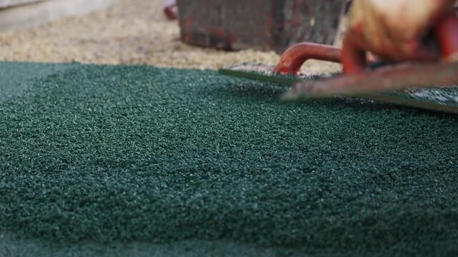 Worker smoothing rubber crumb flooring with hand trowel during installation
