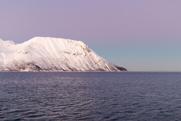 Snowy coastal mountain sloping into calm fjord at twilight in Northern Norway © Alberto