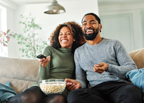 Portrait of a happy young couple watching tv together at home. Shot of a couple resting on the couch watching television