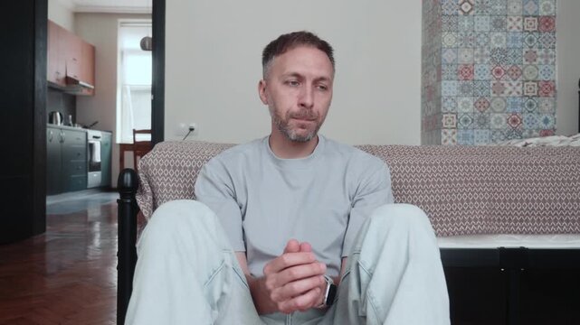AI job loss leaves unemployed man anxious about future, sitting on bedroom floor wringing hands, struggling with financial uncertainty and workplace automation.