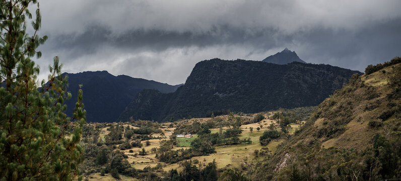Paisaje de colinas rurales con casas dispersas y cordillera de monta&ntilde;as bajo cielo nublado