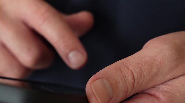 Macro of a man&rsquo;s hands holding a black smartphone, index finger hovering above the screen ready to tap, against a dark navy sweater. A close up for using a phone, choosing an option, hesitating befor