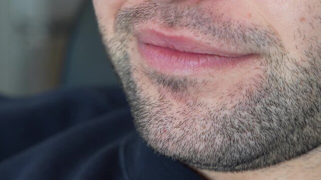 A man with a stubble beard breaks into a broad, toothy smile, his face cropped from the nose down above a navy sweater. A close up for happiness, joy, a positive attitude, dental care, white teeth an