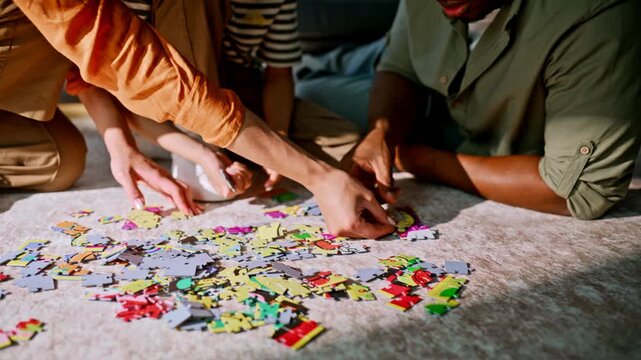 Mixed race family solving jigsaw puzzle living room floor. Closeup hands pieces.