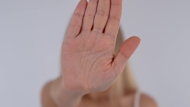 Young blonde woman showing a stop gesture with raised palm, expressing refusal, boundary, rejection and personal protection
