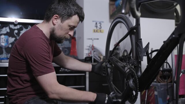 Professional male mechanic fixing expensive black carbon road bike in specialized workshop. Technical service of high-end racing bicycle components, drivetrain tuning and high-precision maintenance.