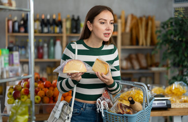 Female shopper with grocery cart choosing fresh cheese for Christmas or New Year celebration in...