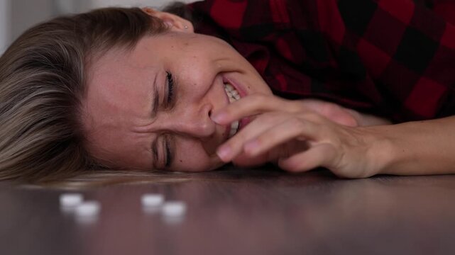 Young blonde woman lies on the floor crying beside scattered pills, portraying severe emotional breakdown, despair and a dangerous medication misuse concept in a mental health emergency
