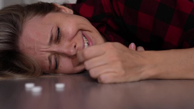 Young blonde woman cries beside scattered pills and reaches for one in hesitation, portraying despair, emotional crisis and the concept of dangerous medication misuse