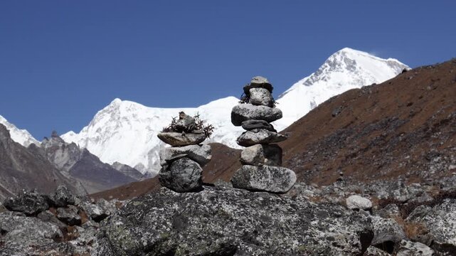 Two balanced stone cairns standing in a rocky landscape with the majestic snow-capped peaks of the himalayas under a clear blue sky, symbolizing harmony, stability and spirituality