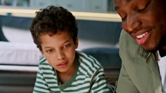 Closeup boy writing homework pen. African american dad helping son study home.