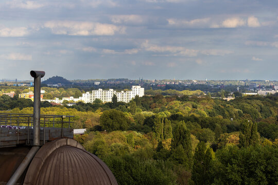 High-angle urban landscape from industrial rooftop dome over green forest canopy white residential apartment blocks slag heap hill and skyline horizon in Duisburg Ruhr region