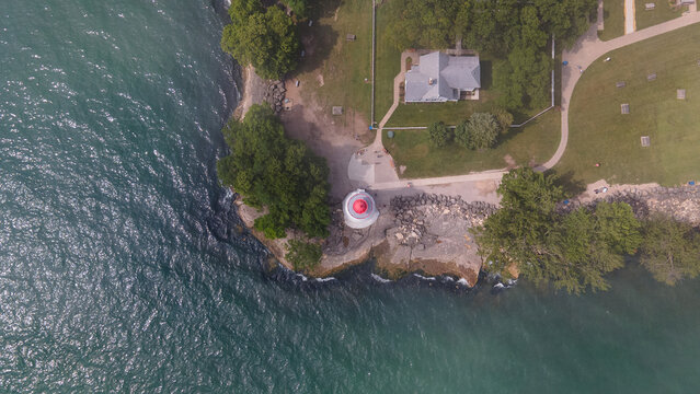 Lakeside Marblehead, United States - 10 June 2021: Aerial view of Marblehead Lighthouse on the rocky shoreline of Lake Erie, surrounded by lush green trees and a historic keeper's house.