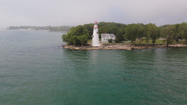 Lakeside Marblehead, Ohio, United States - 10 June 2021: Aerial view of Marblehead Lighthouse on the rocky Lake Erie shoreline, surrounded by green trees and a white keeper's house.