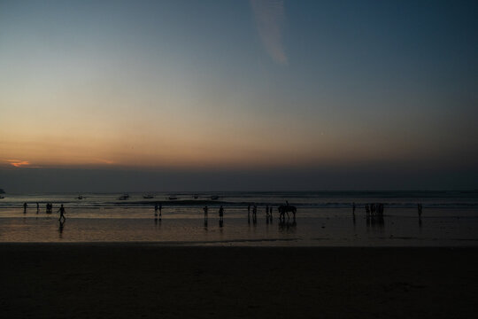 Silhouetted people walking on a tropical sandy beach during a dramatic sunset ocean view.