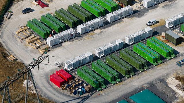 Saleux, France - 08 July 2026: Aerial view of a battery energy storage system site featuring rows of green and white industrial containers, power infrastructure, and utility cables on a gravel ground.