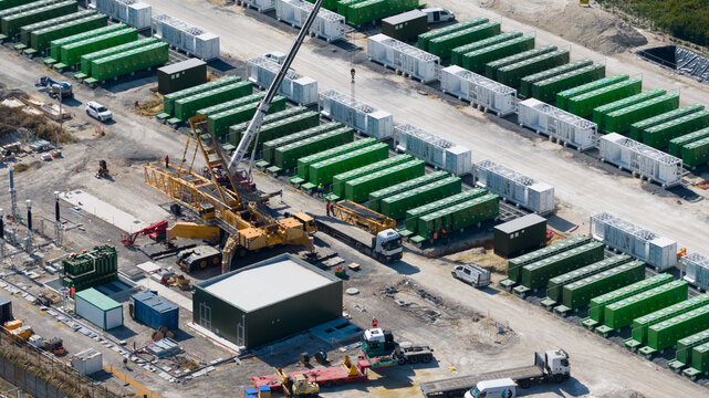 Saleux, France - 08 July 2026: Aerial view of a battery energy storage system construction site featuring rows of green containers, a mobile crane, and construction vehicles.