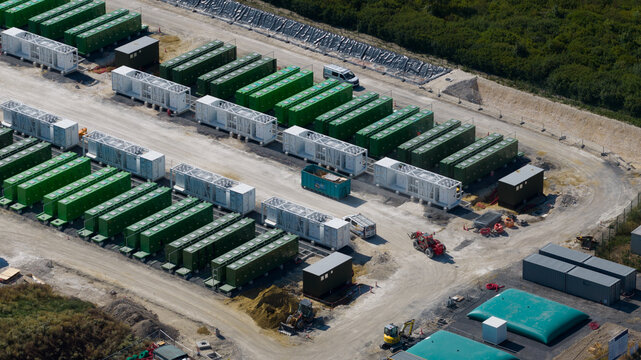 Saleux, France - 08 July 2026: Aerial view of a large battery energy storage system site featuring rows of green and white shipping containers, construction vehicles, and industrial equipment.