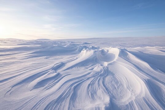 Snowdrifts with smooth wind sculpted patterns stretching across a vast frozen tundra under a clear blue sky.
