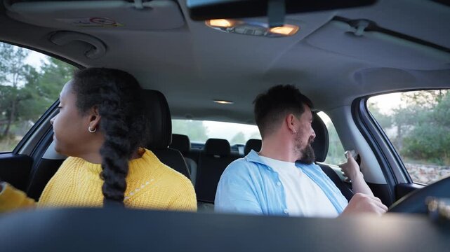 A Caucasian man and a Latina African American woman enter a car, sit in the front seats and fasten their seat belts. They settle into position, exchange smiles and prepare for a journey