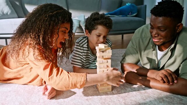Family lying floor playing wooden block tower game. Parents child clapping home.