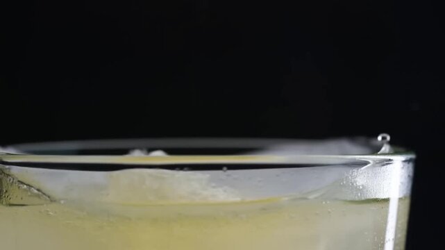 Carbonated yellow drink fizzing in a clear glass against a dark background