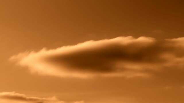 Lenticular cloud holds its rounded shape above layered clouds in an amber sky