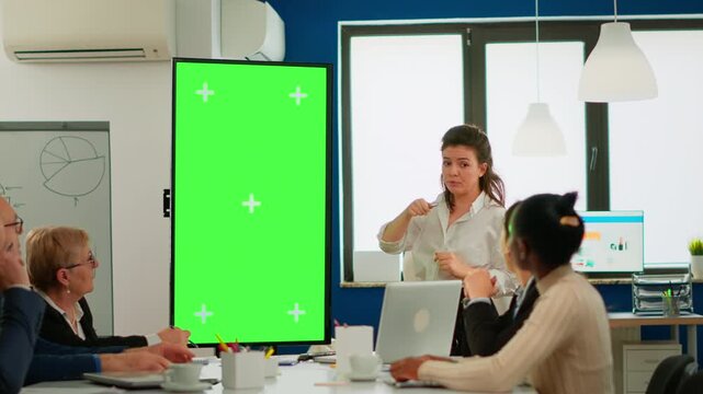 Greenscreen, businesswoman and training with presenter pointing at a vertical chroma key screen while colleagues watch, for office briefing, project planning, teamwork, communication and custom media.
