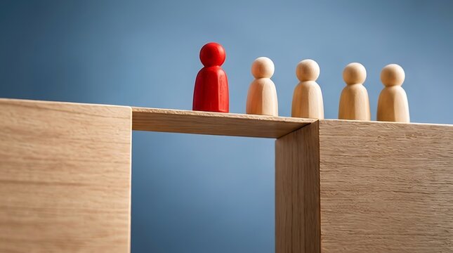 Leadership and business strategy concept with a unique red wooden figure leading a group of followers across a bridge over a gap between two blocks to achieve success and overcome obstacles.