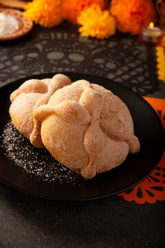 Traditional Mexican Pan de Muerto sweet breads on a matte black plate next to a festive orange papel picado paper cutout for Day of the Dead.