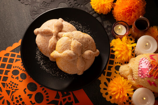 Traditional Mexican Altar, Pan de Muerto sweet bread on a black plate, placed on a Day of the Dead altar setup with cempasuchil marigold flowers and sea salt background.