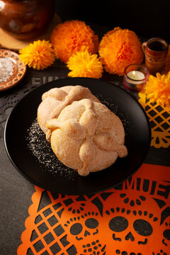 Traditional Mexican Altar, Pan de Muerto sweet bread on a black plate, placed on a Day of the Dead altar setup with cempasuchil marigold flowers and sea salt background.