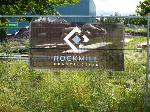 Gloucester, Ontario, Canada &ndash; August 03, 2025: A "Rockmill Construction" mesh banner is attached to a temporary chain-link fence surrounding an outdoor construction site with wild vegetation on Sheffo
