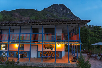 traditional Colombian house in the Coffee Region stands against the backdrop of a massive mountain, with the sky providing a striking contrast to the vivid colors of the architecture © juanjos
