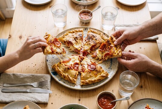 Top down flat lay of two people sharing a warm calzone meal at a bright dining table. Clean daylight visual style for casual dining and app ads.