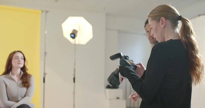 Diverse crew asst entering moving strobe while pro prepping cam and model posing on yellow backdrop