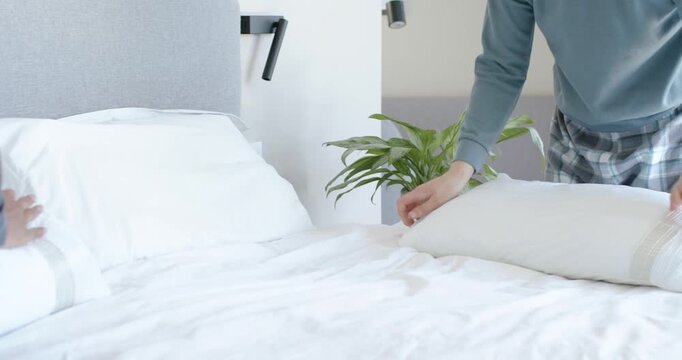 African American man approaching bed in bedroom tidying bedding, fluffing pillow