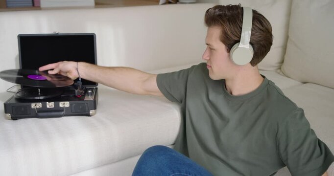 Seated adult male inspecting record, placing it on turntable, wearing headphones