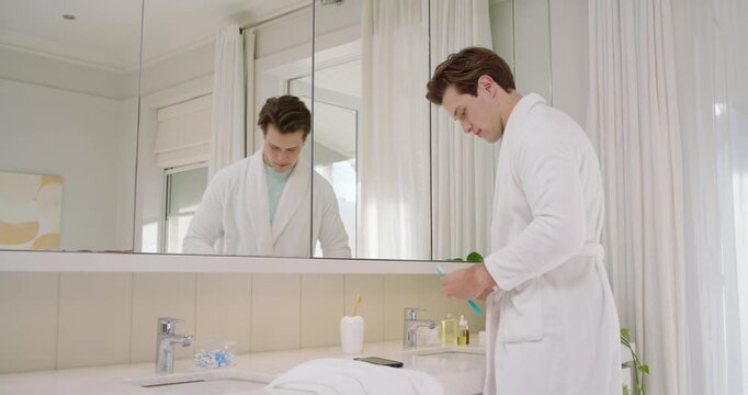 Adult male in robe entering frame loading blue brush turning faucet brushing teeth for morning care