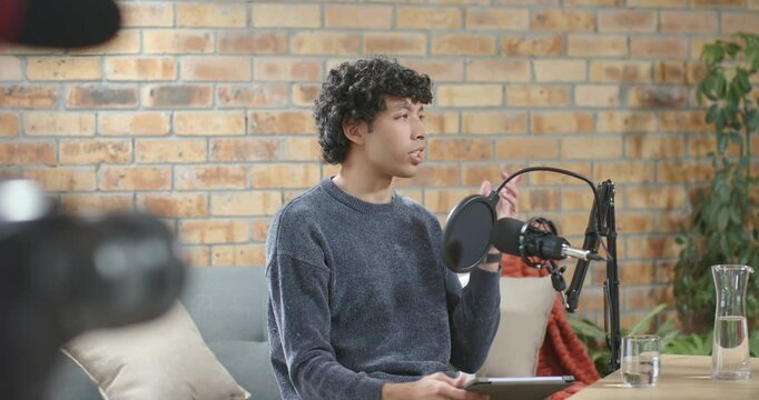 African American man sitting on sofa holding tablet speaking into mic during podcast after host cue