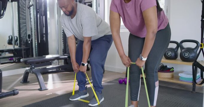 African couple stepping on resistance bands, pulling rowing motion in home gym building strength