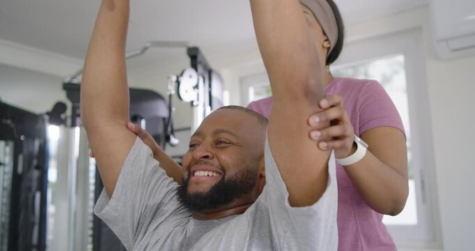 African American pair pressing dumbbells on bench at home, spotter bracing elbows to finish set