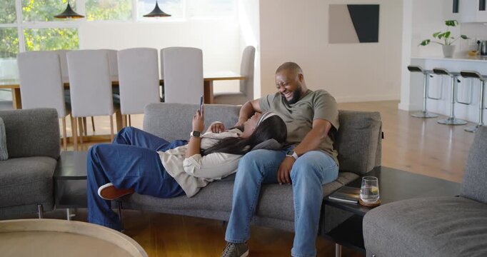African American couple lounging on sofa, woman scrolling phone to share while man stroking hair