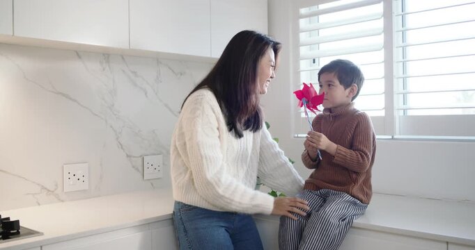 Asian mother in white sweater and child sitting in kitchen, mother tapping red pinwheel teaching
